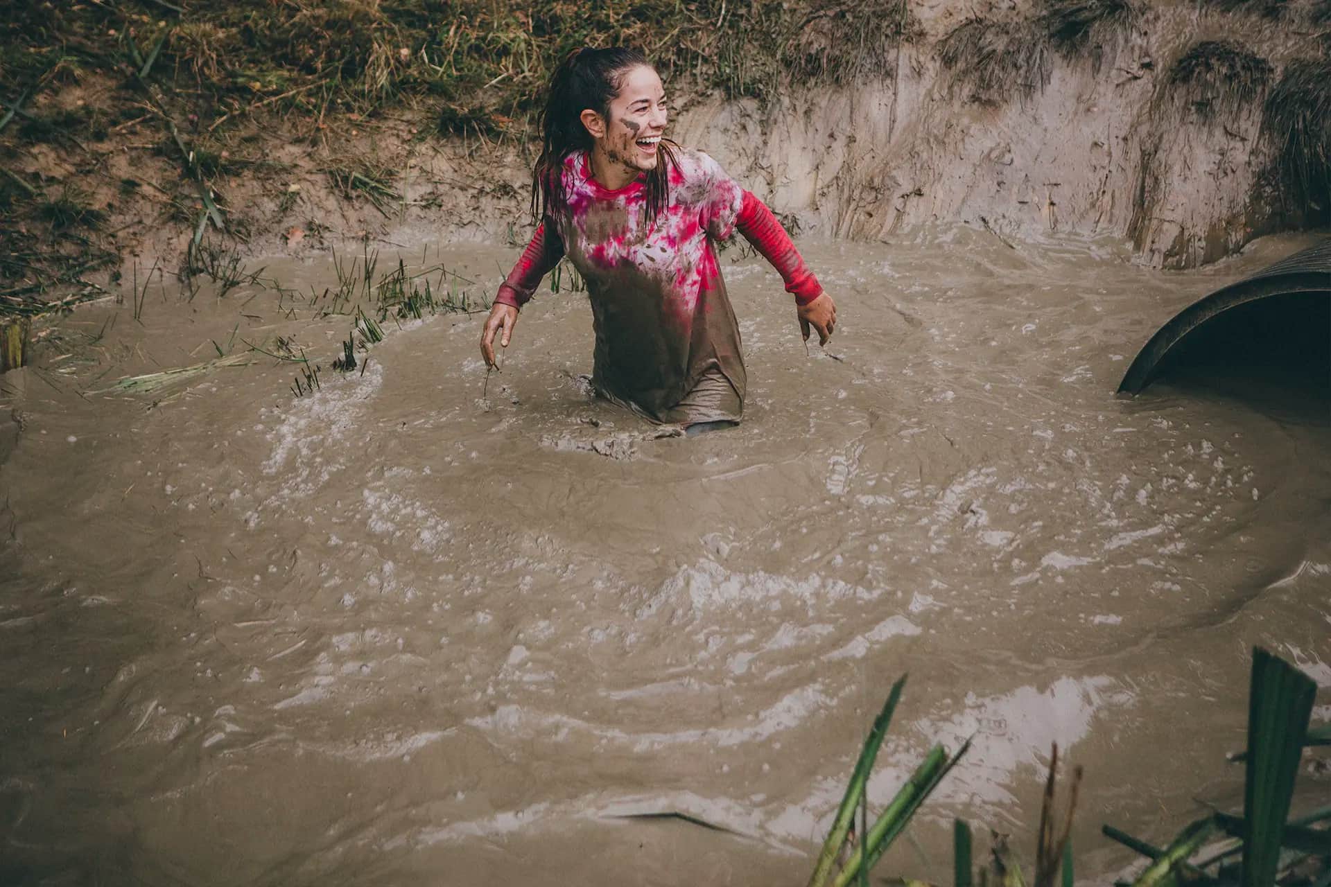 A woman in a muddy pool up to her waist in water, laughing.