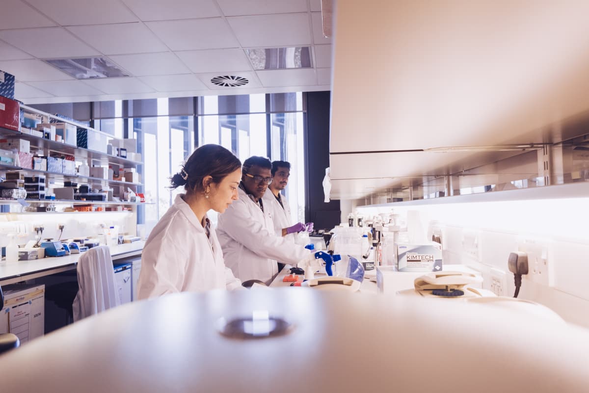 Three researchers wearing Cancer Research UK branded lab coats.