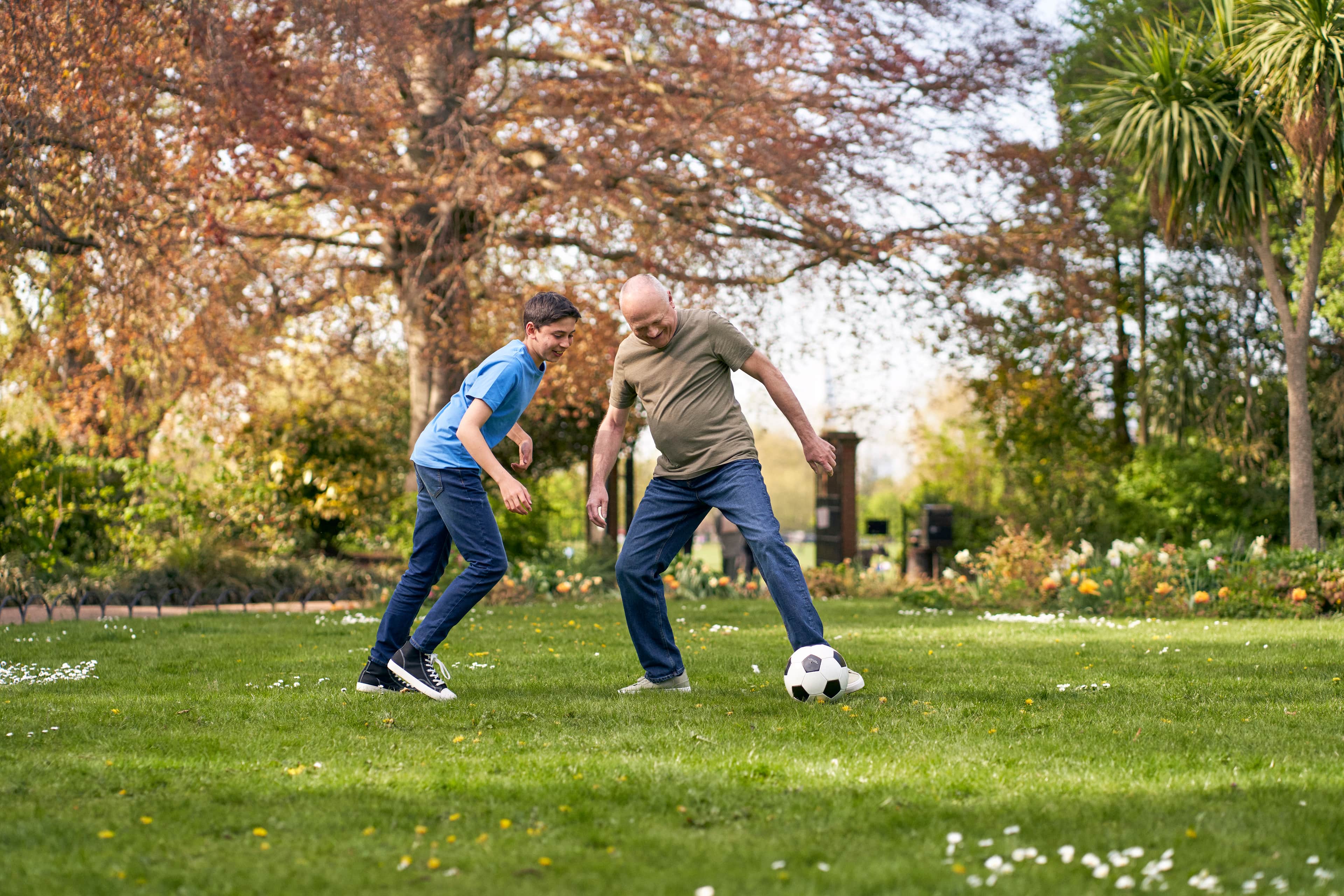Man and young boy playing football together in a park.
