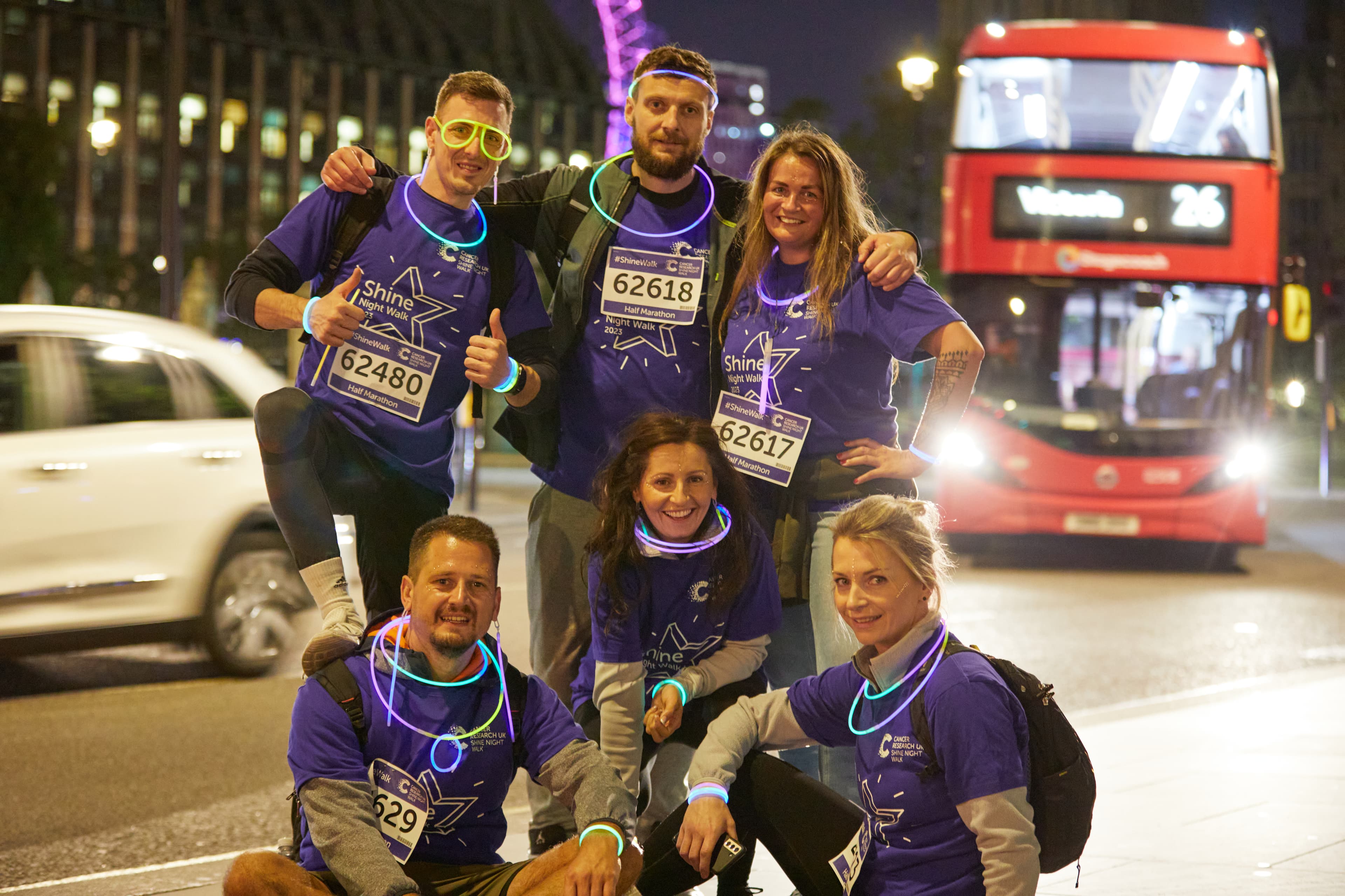 5 smiling shine night walk participants pose for a photo at night on a London street. Double-decker bus in the background.