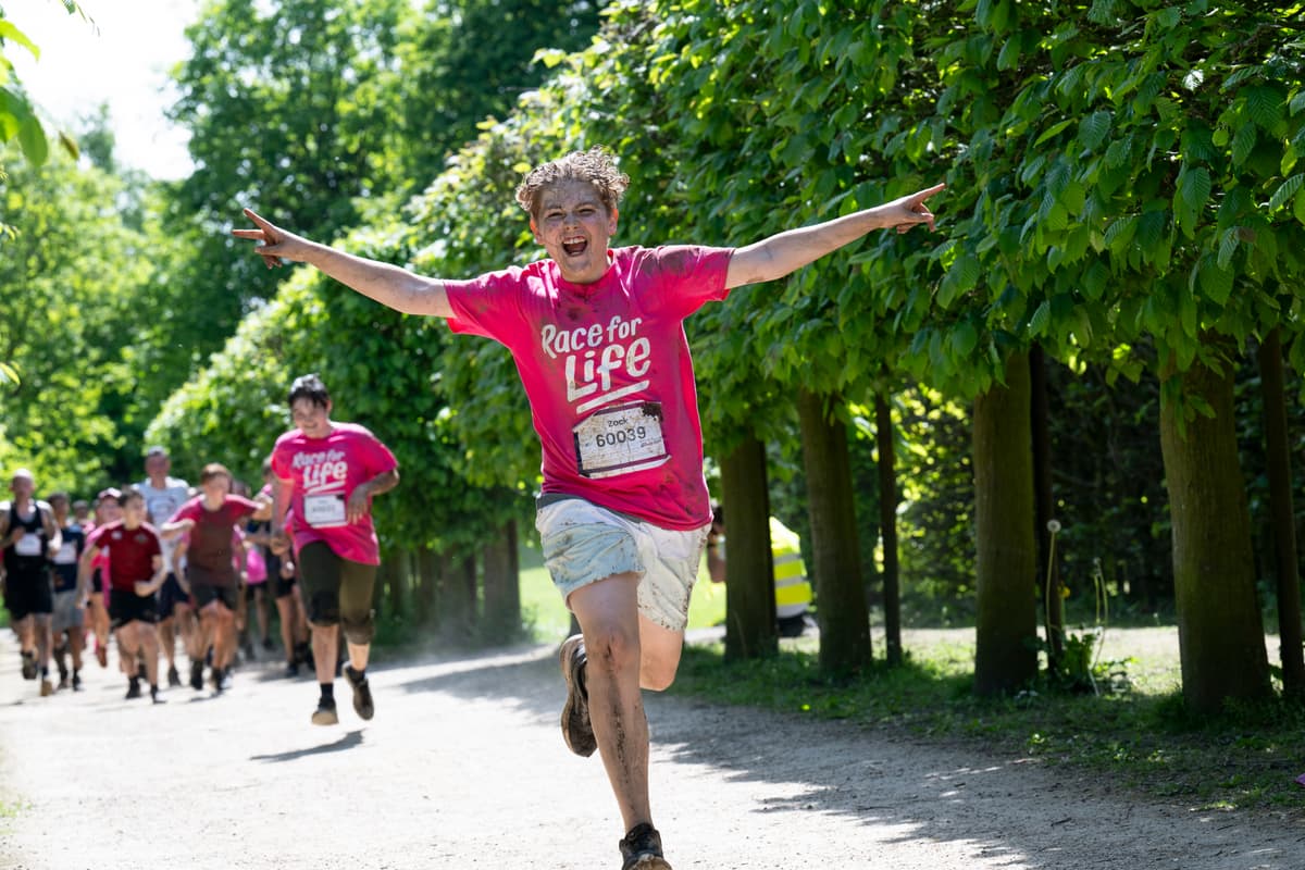 Boy wearing a Race for Life T-shirt, running covered in mud during the CRUK Tough Mudder event.