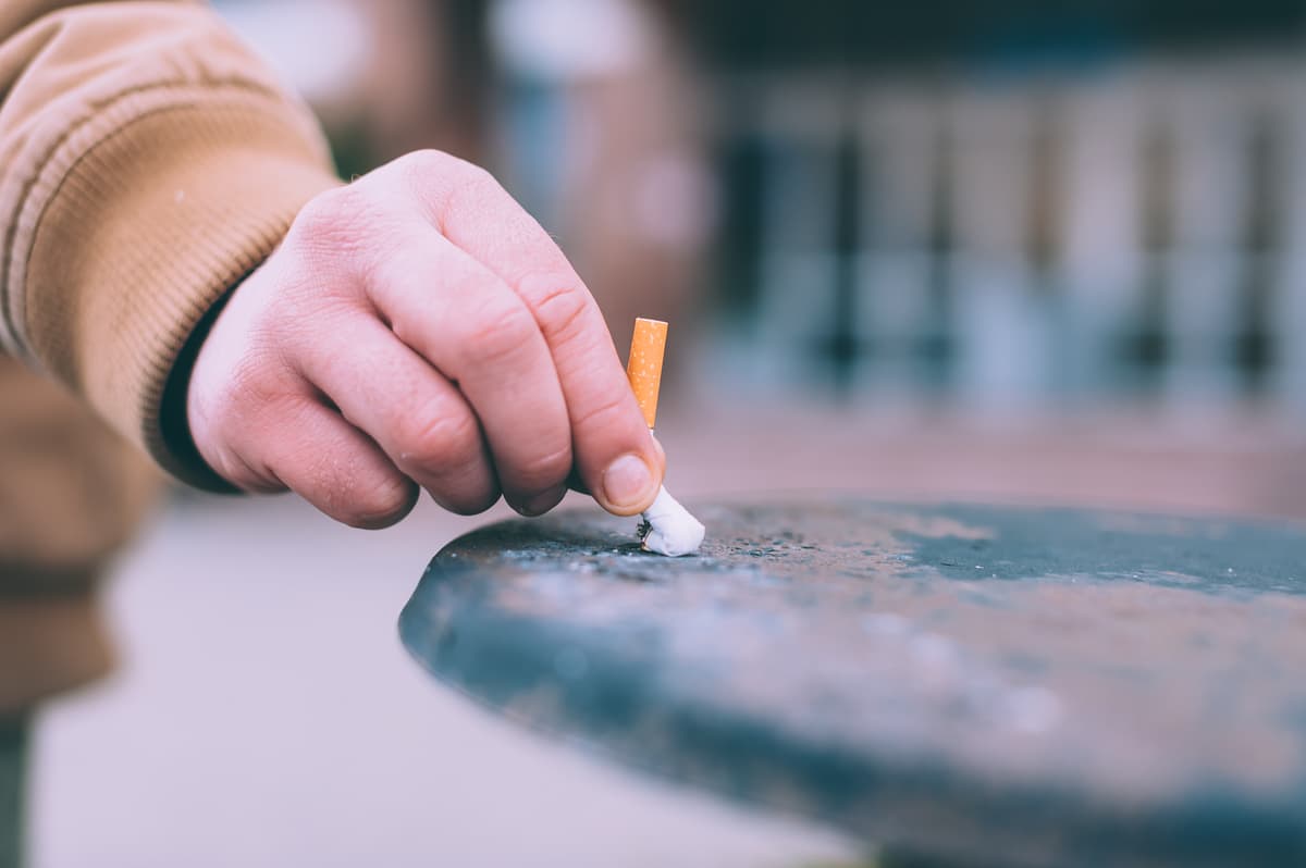 A man puts out a cigarette in the trash.