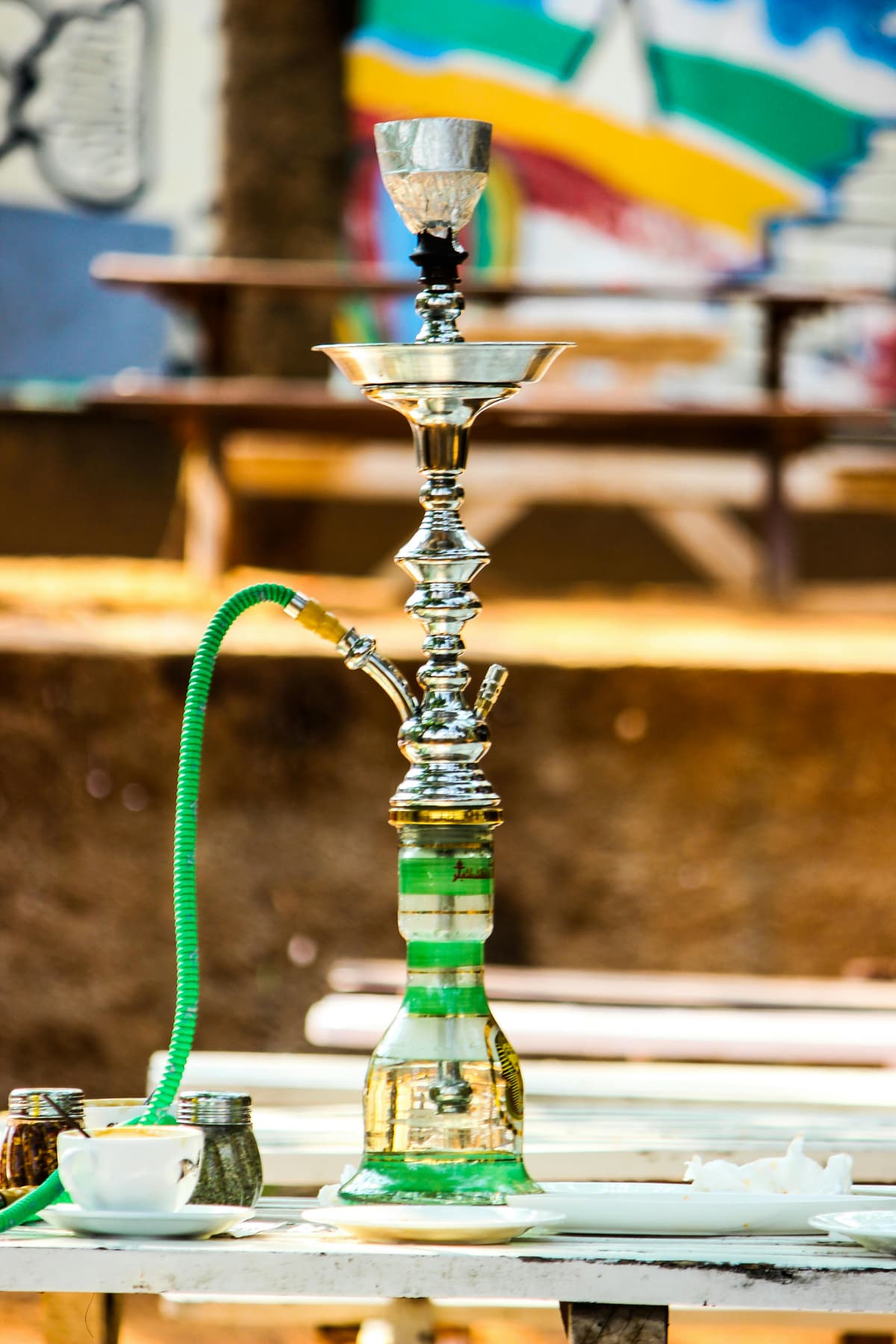 A hookah with a green hose and gold-and-silver body is placed on an outdoor table.