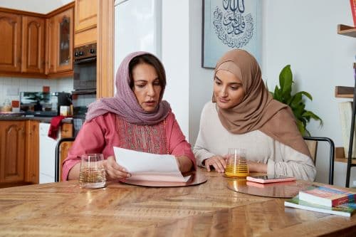 Two women sat at home looking at a letter.