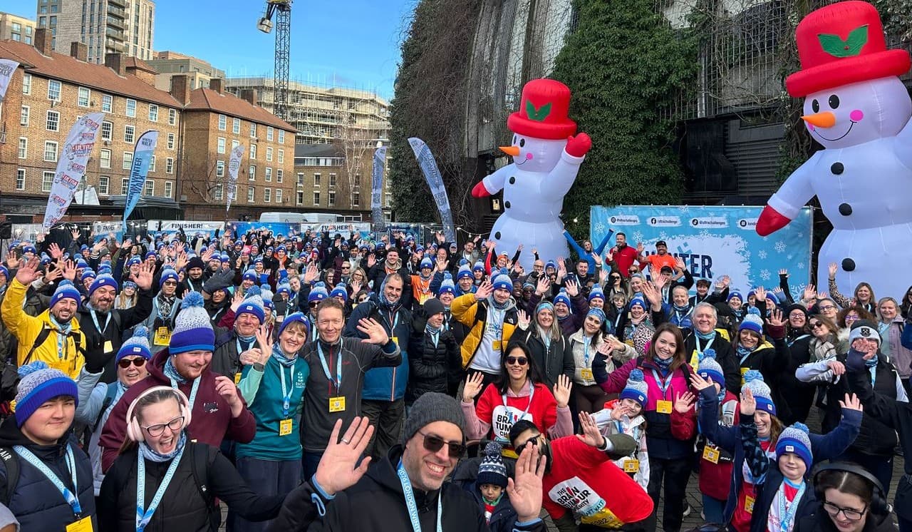 Large group of participants gathered at a winter charity event, waving at the camera in London with 2 inflatable snowmen.