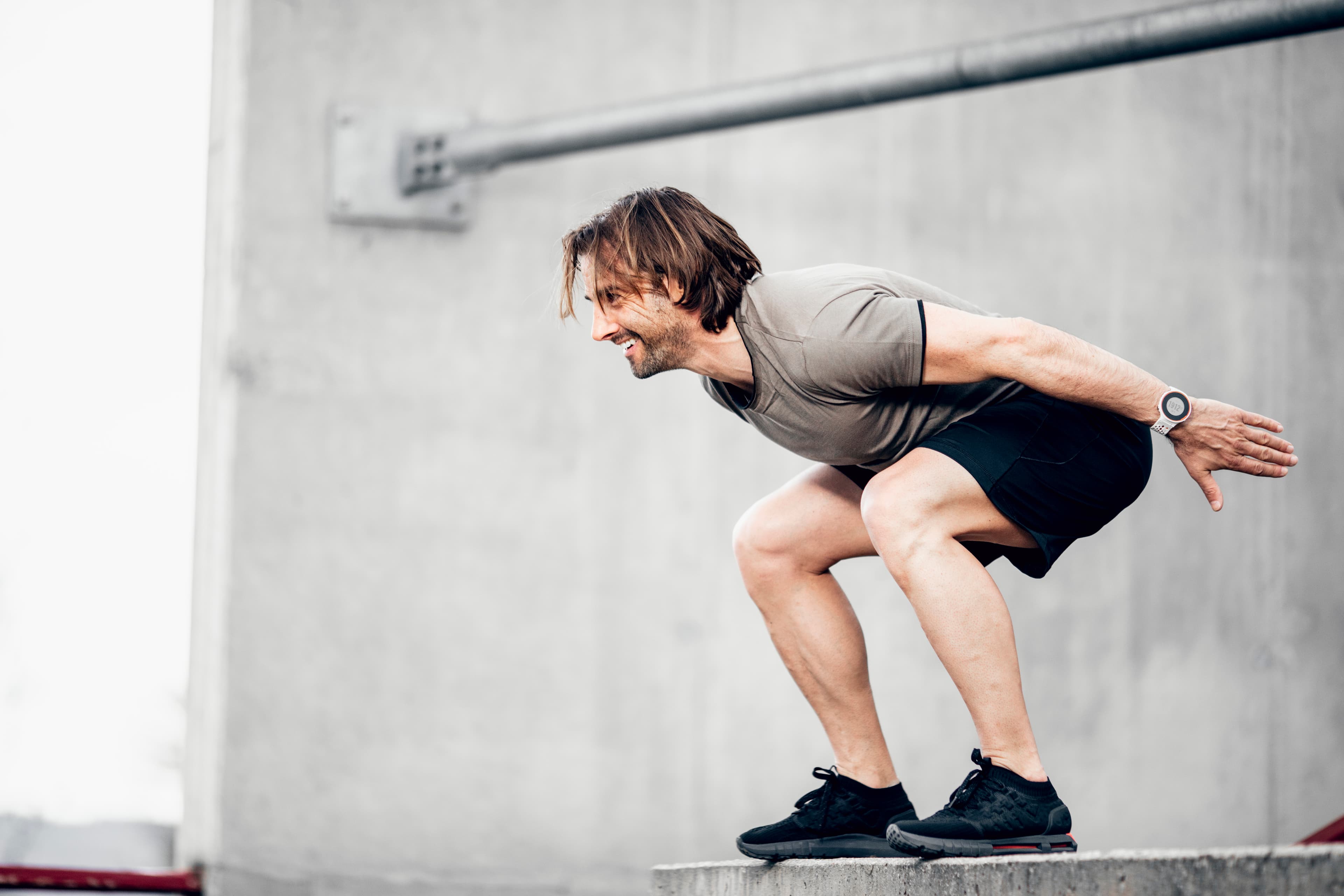 Side-shot of a man doing a squat with his arms back and smiling.