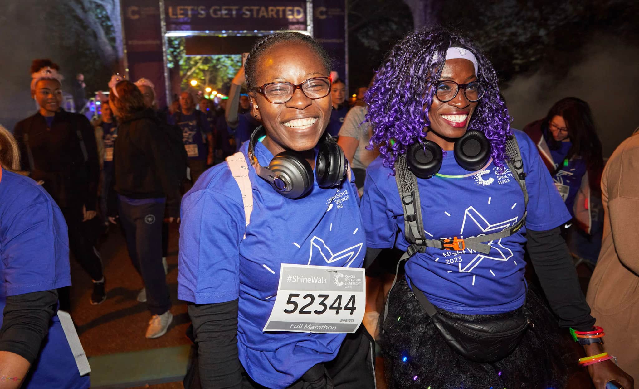Two women wearing Shine Night Walk t-shirts standing near the start line and smiling.