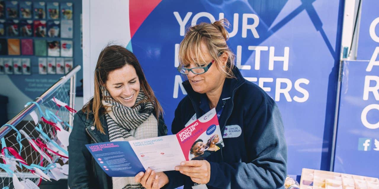 A photo showing a volunteer from Cancer Research UK talking to a member of the public.