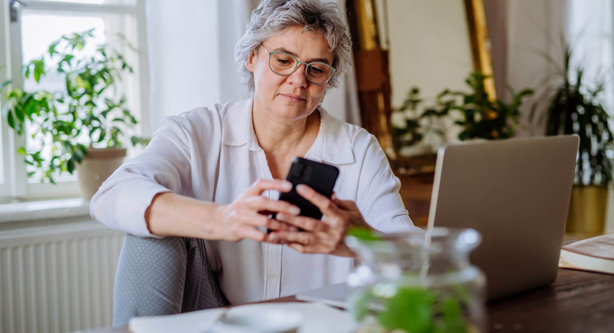 Image shows volunteer sat at a table using mobile phone and laptop.