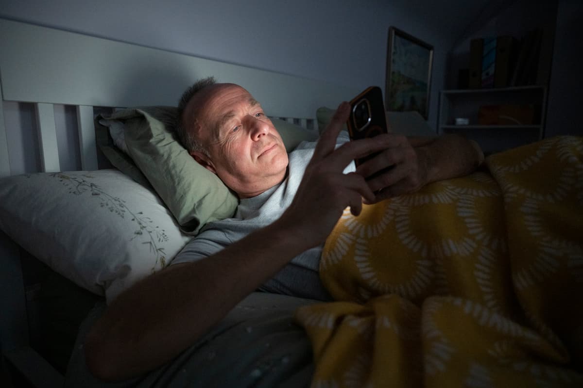 The image is of a man lying in bed using his phone.