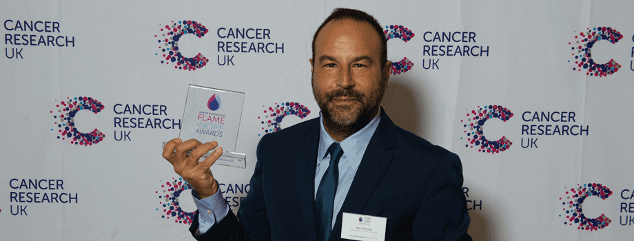 Photo of Alim holding an award in front of a cancer research background.