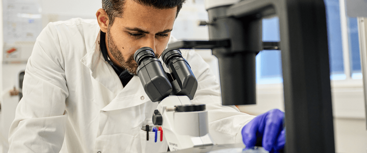 A scientist looking down a microscope.