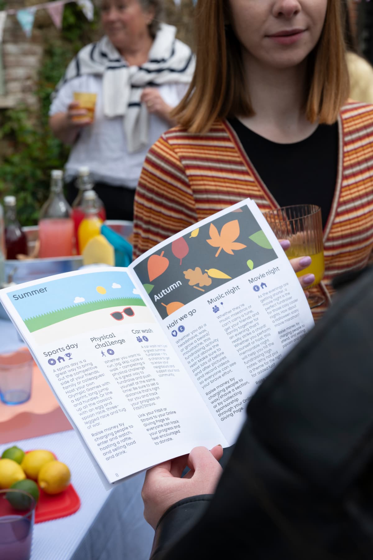 Person holding booklet with summer and autumn events at outdoor community gathering.