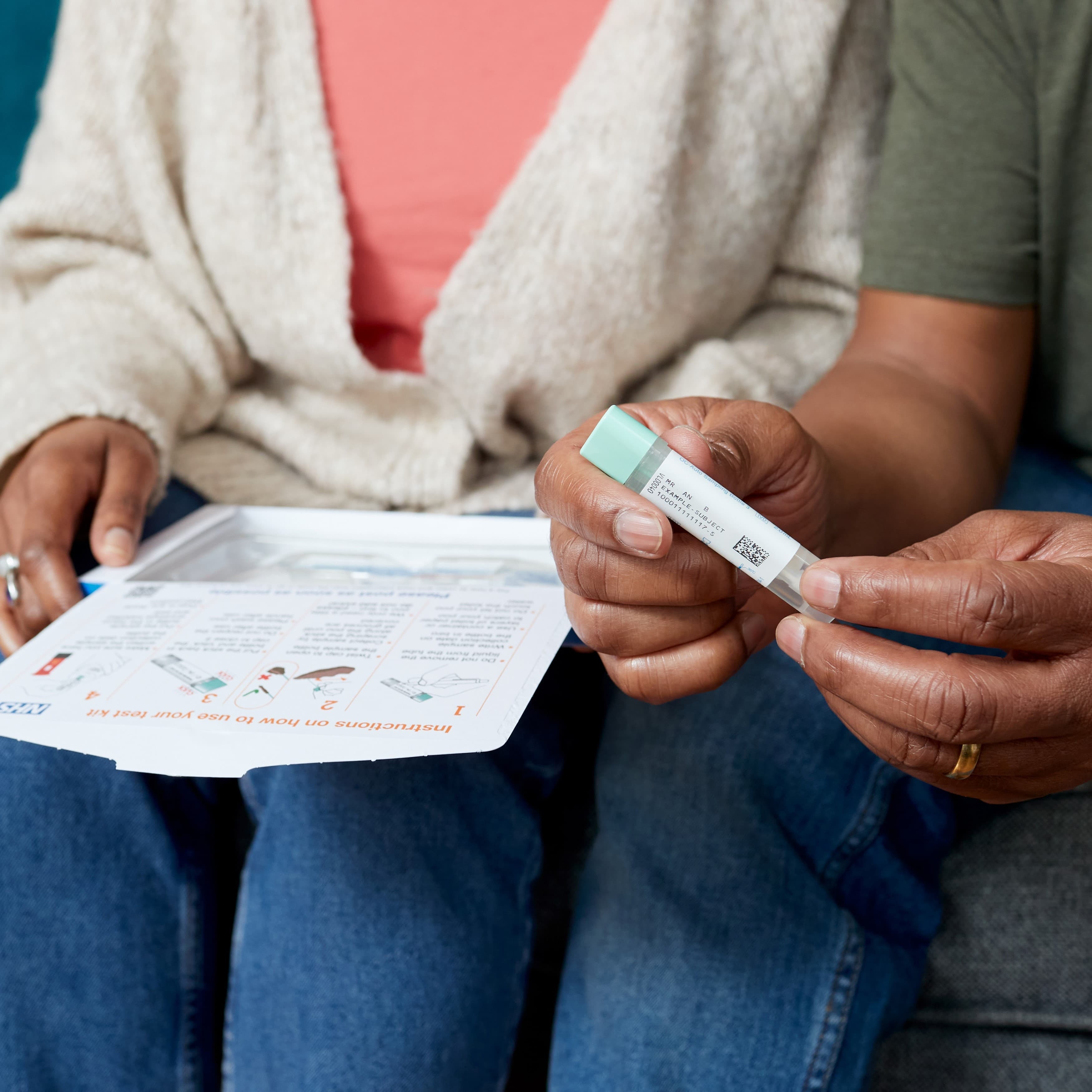 The photo shows a man with his partner on the sofa opening a bowel cancer screening test kit from NHS England.
