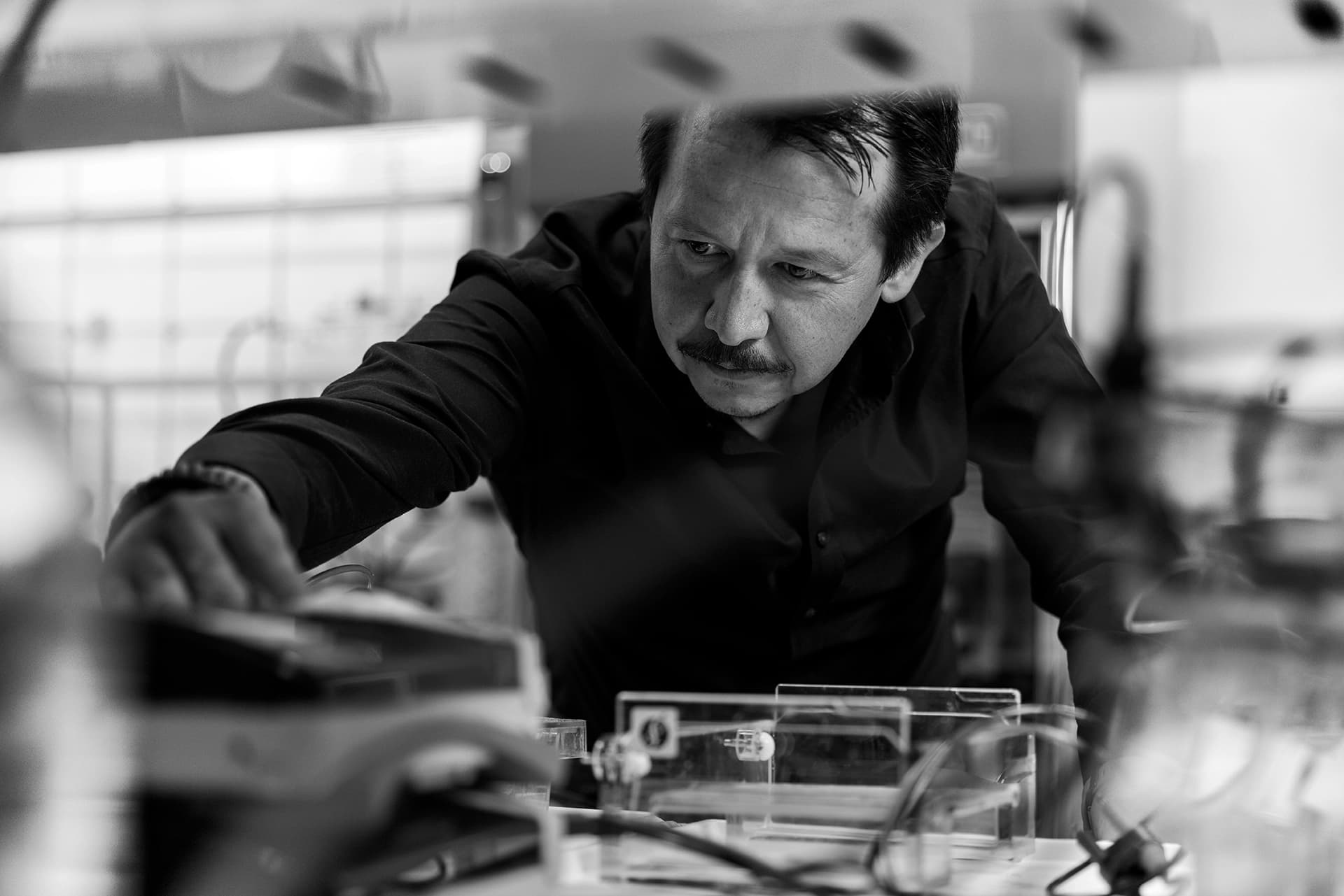 Professor Sergio Quezada reaching across some equipment, checking for something.