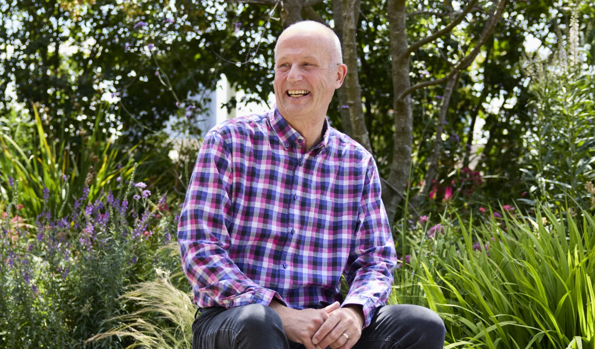 Graeme sits in a garden looking happy.