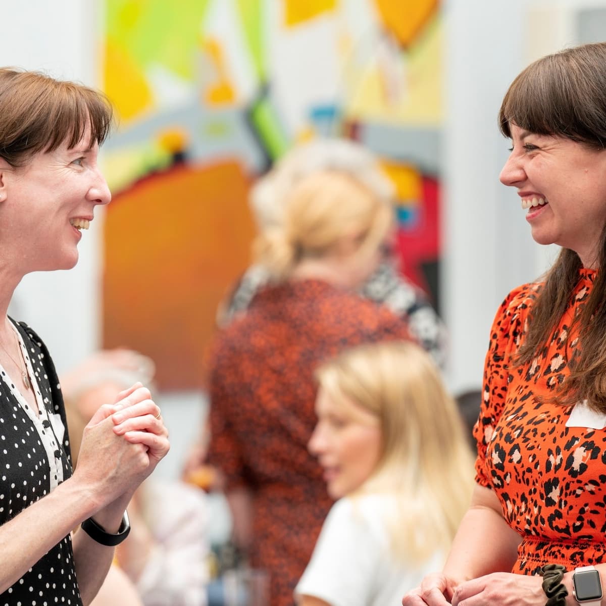 Two women standing in a room facing each other smiling.