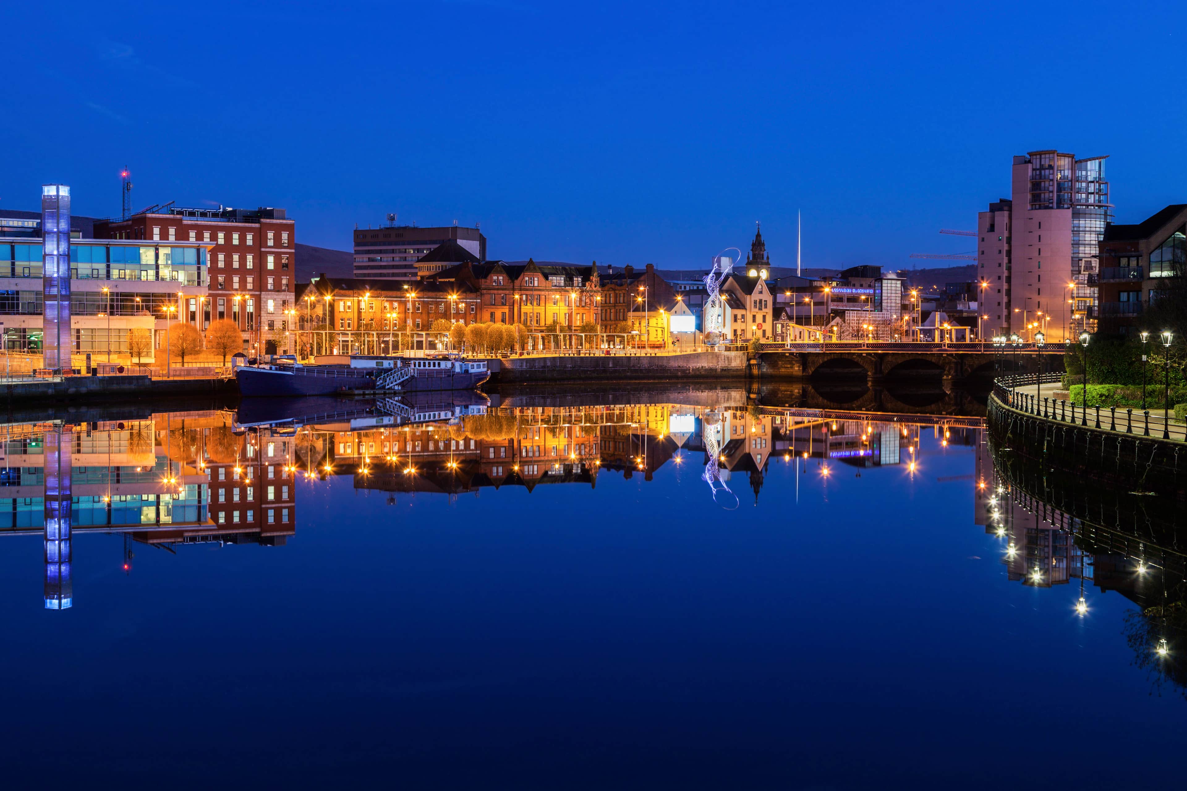 Belfast at night with lights from the buildings reflected in the River Lagan.