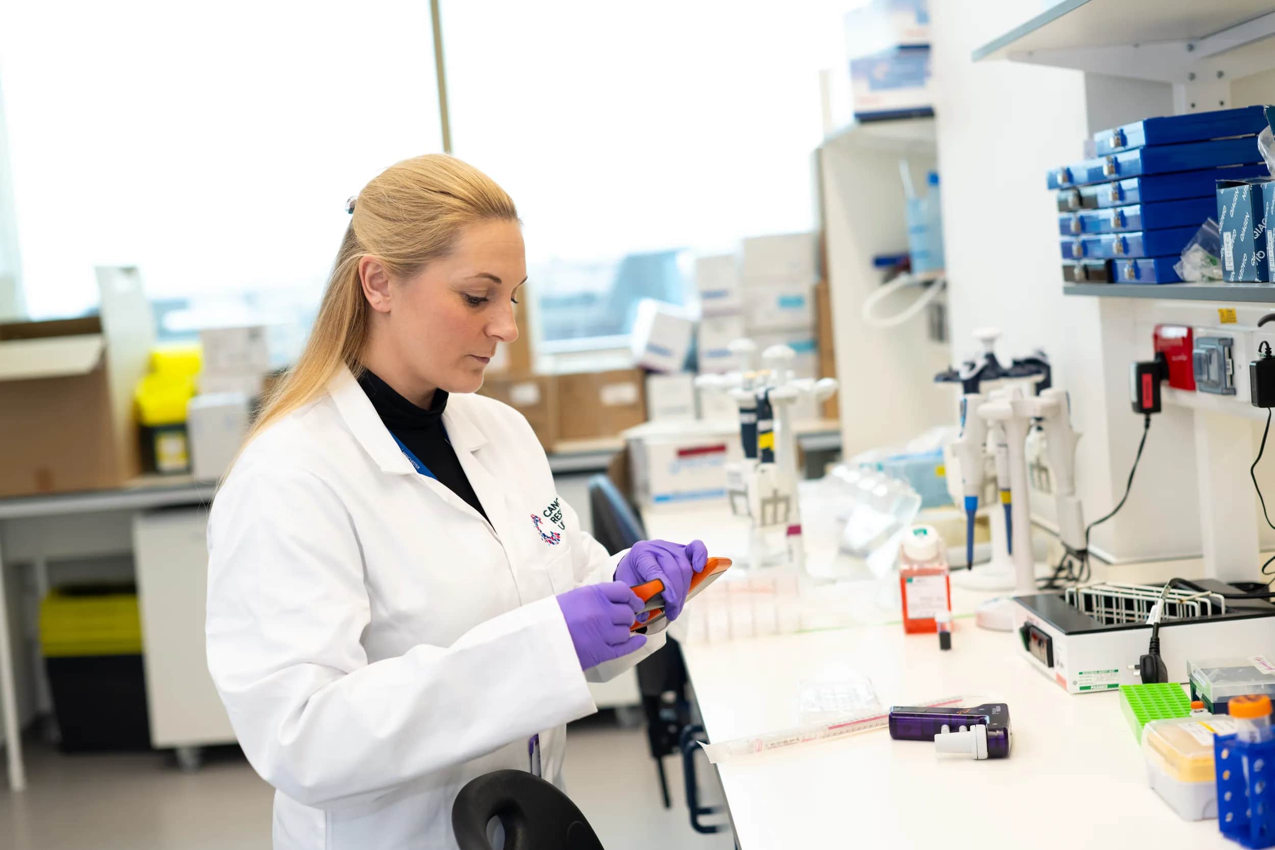 A Cancer Research UK researcher in a lab looking at a device in her hand. She's concentrating and looks determined.
