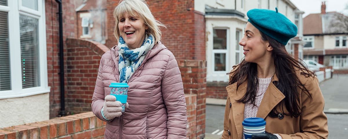 Two women walking down a street holding coffees.