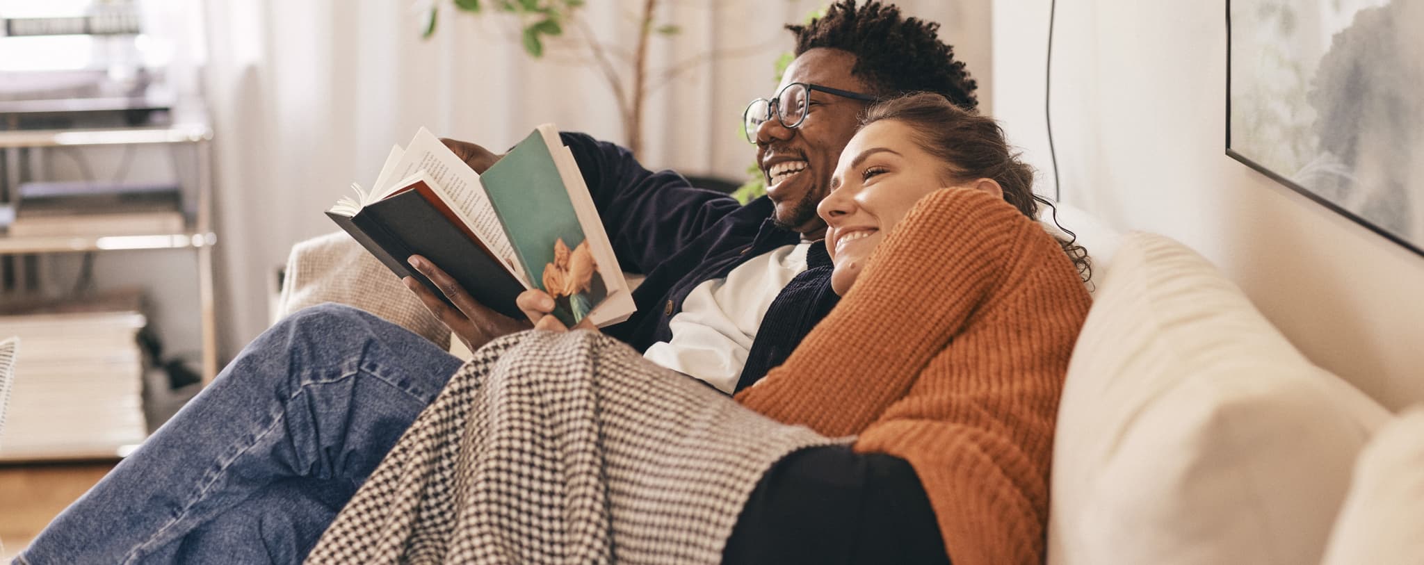 Two people sat on a couch reading books.