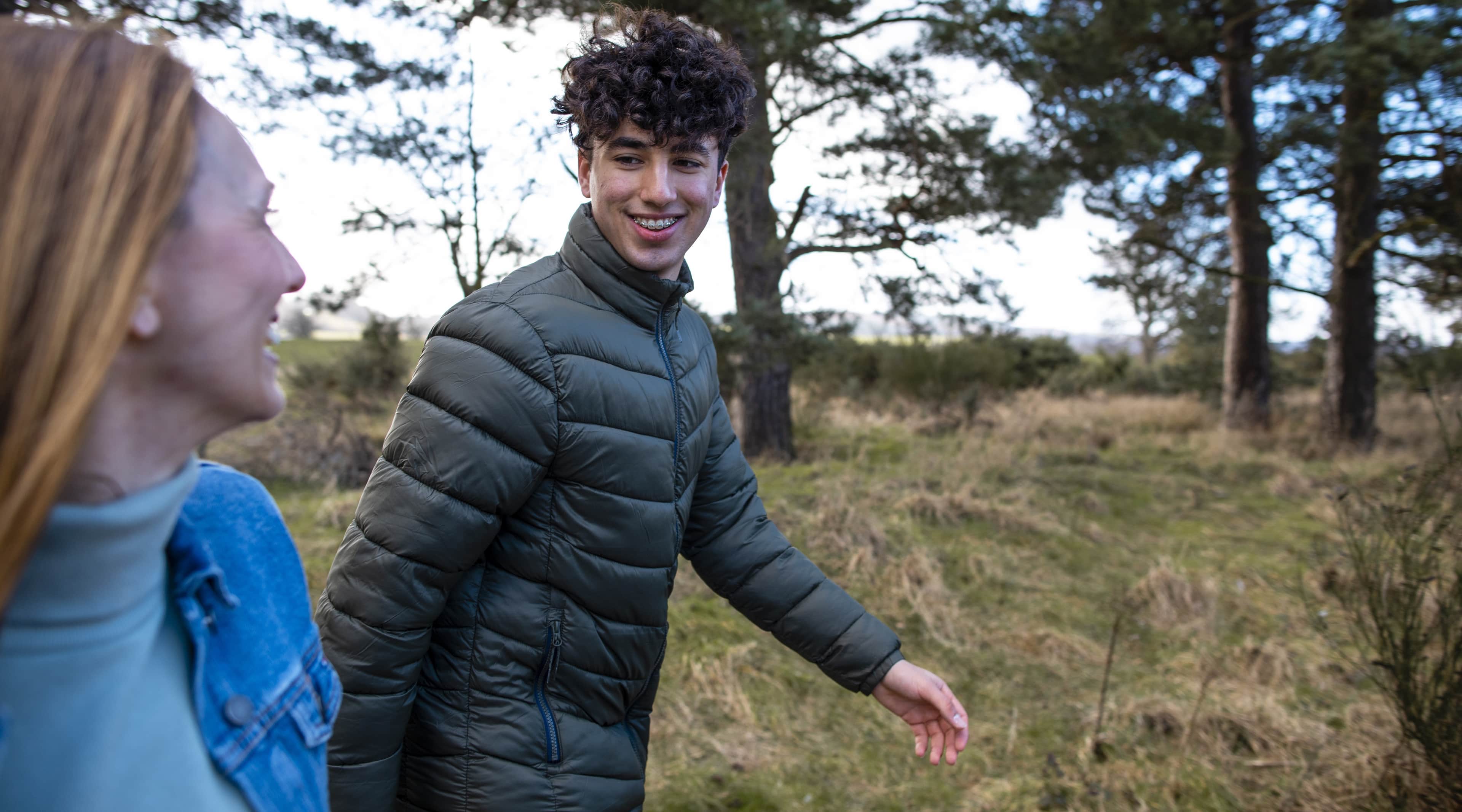 A man and woman smiling walking together through a grassy woodland path.