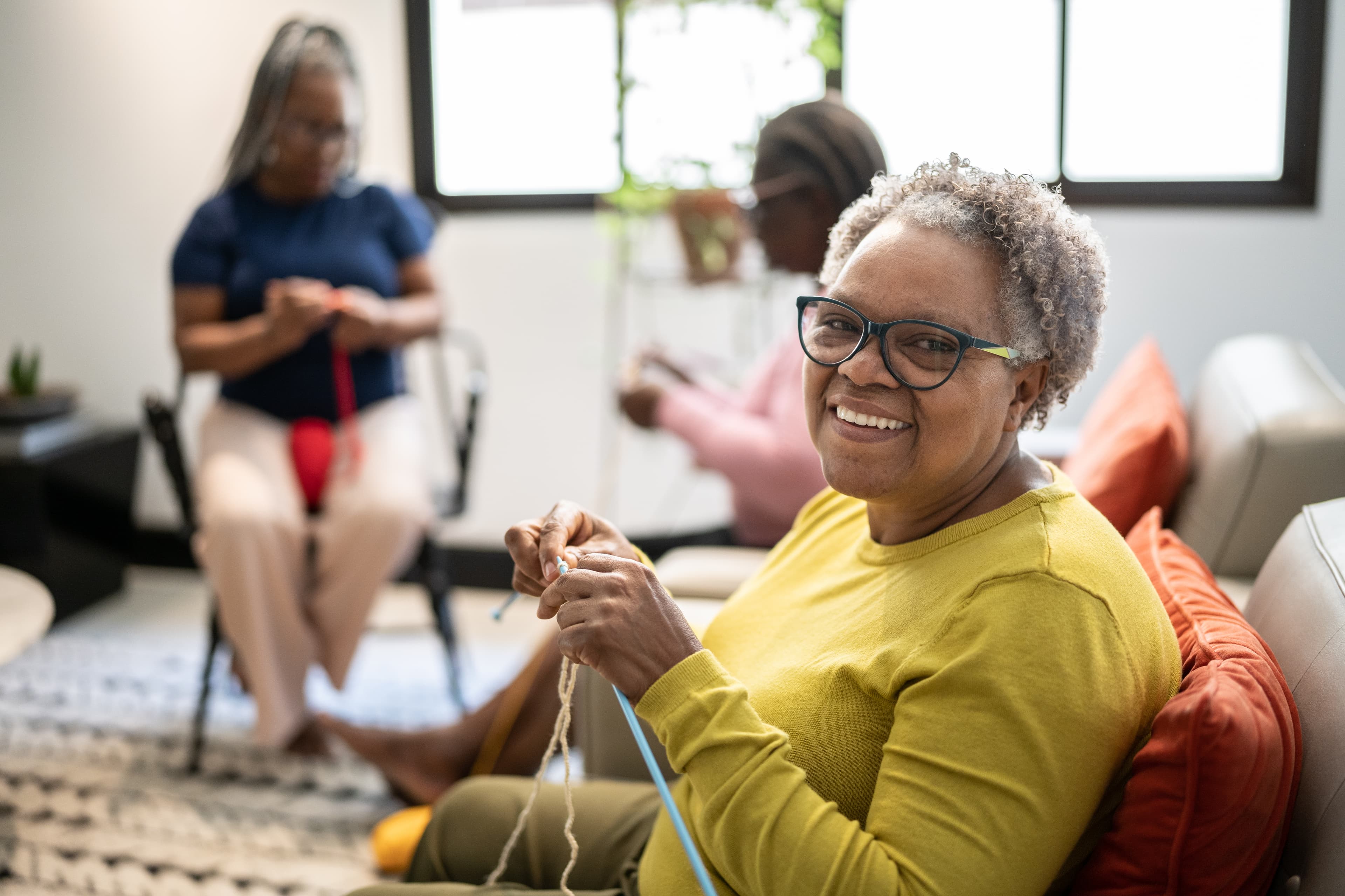 Three people knitting together in a cozy room, smiling and enjoying each other's company.