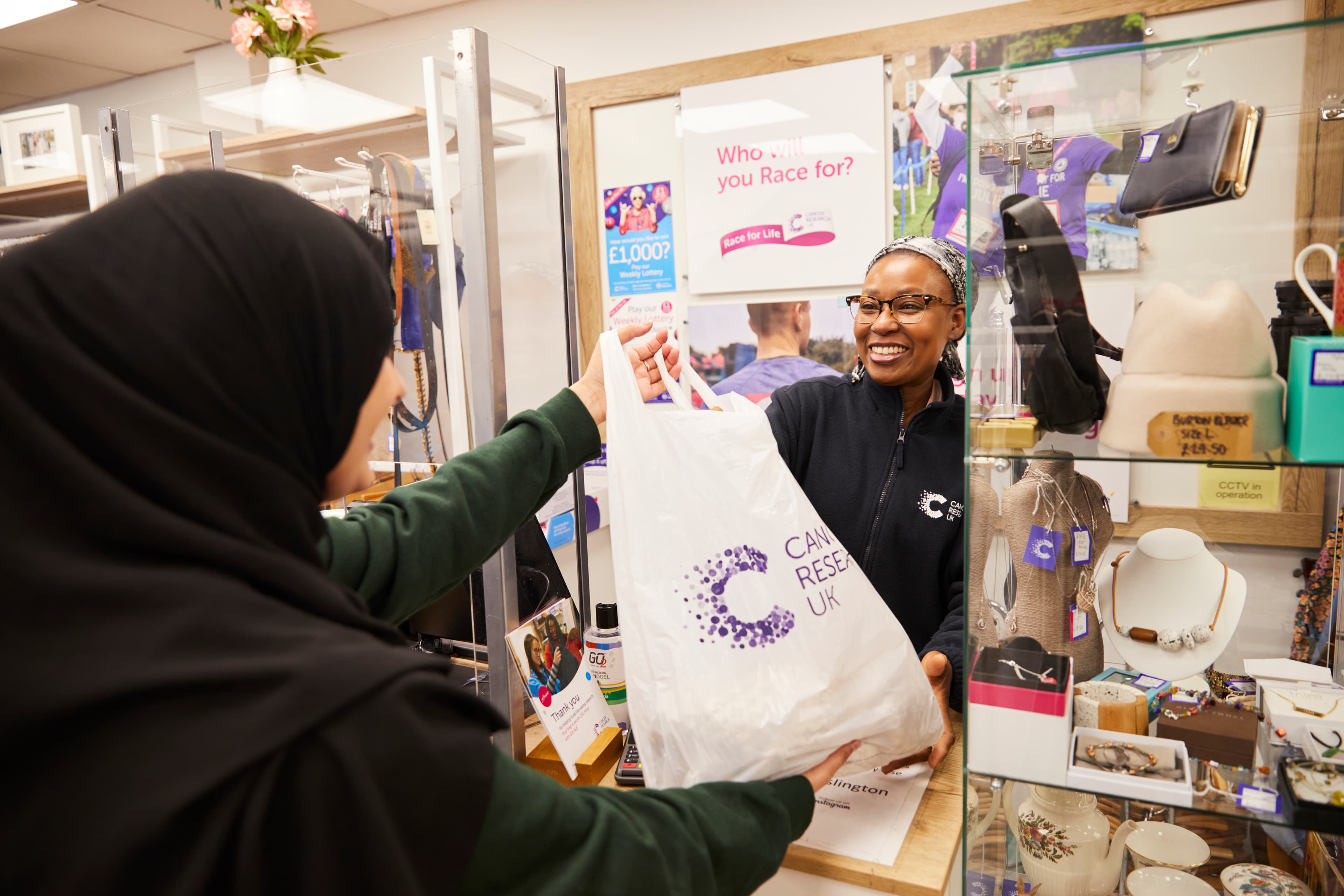 A Cancer Research UK volunteer handing branded bag to a customer in one of our shops.