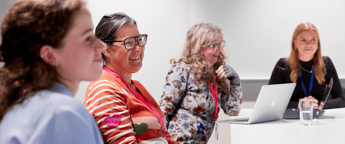 Four people sat at a table in a meeting. They are all smiling.