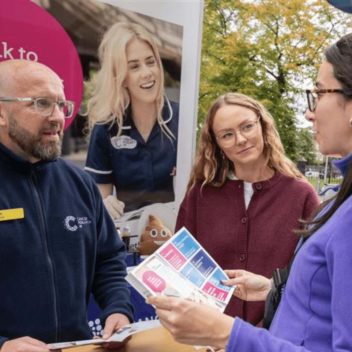 A Cancer Roadshow nurse talks two women through a cancer awareness leaflet in the street.