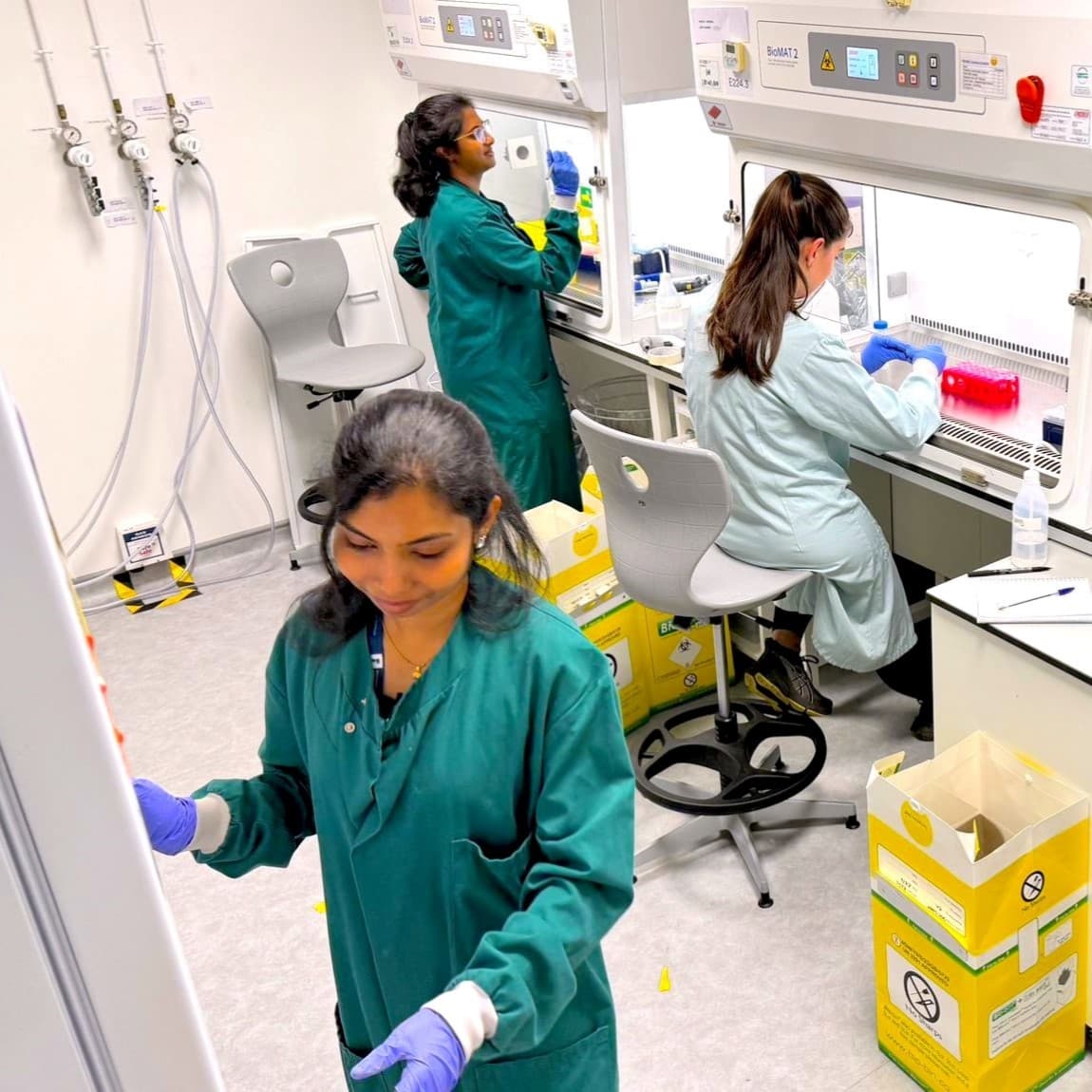 A group of researchers working together in a lab, all in green lab coats.