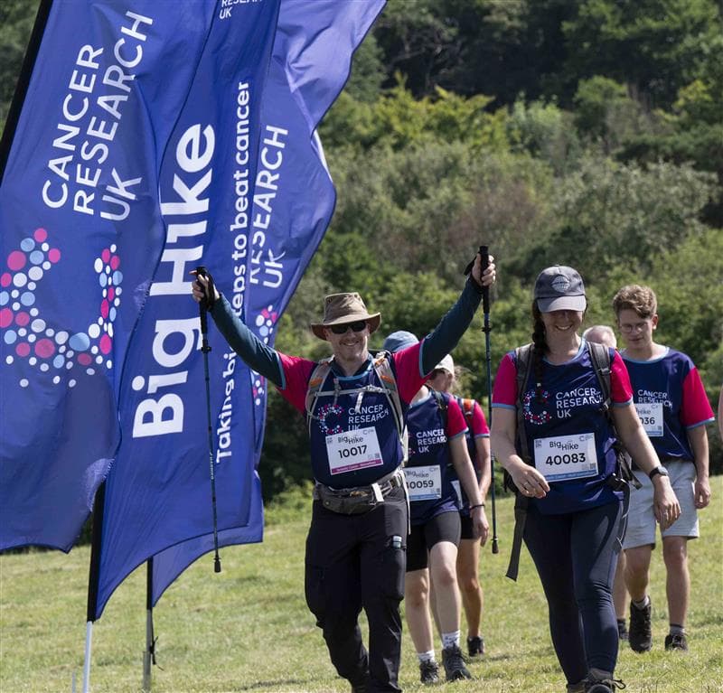 people wearing CRUK branded tops walking in the countryside next to CRUK branded banners.