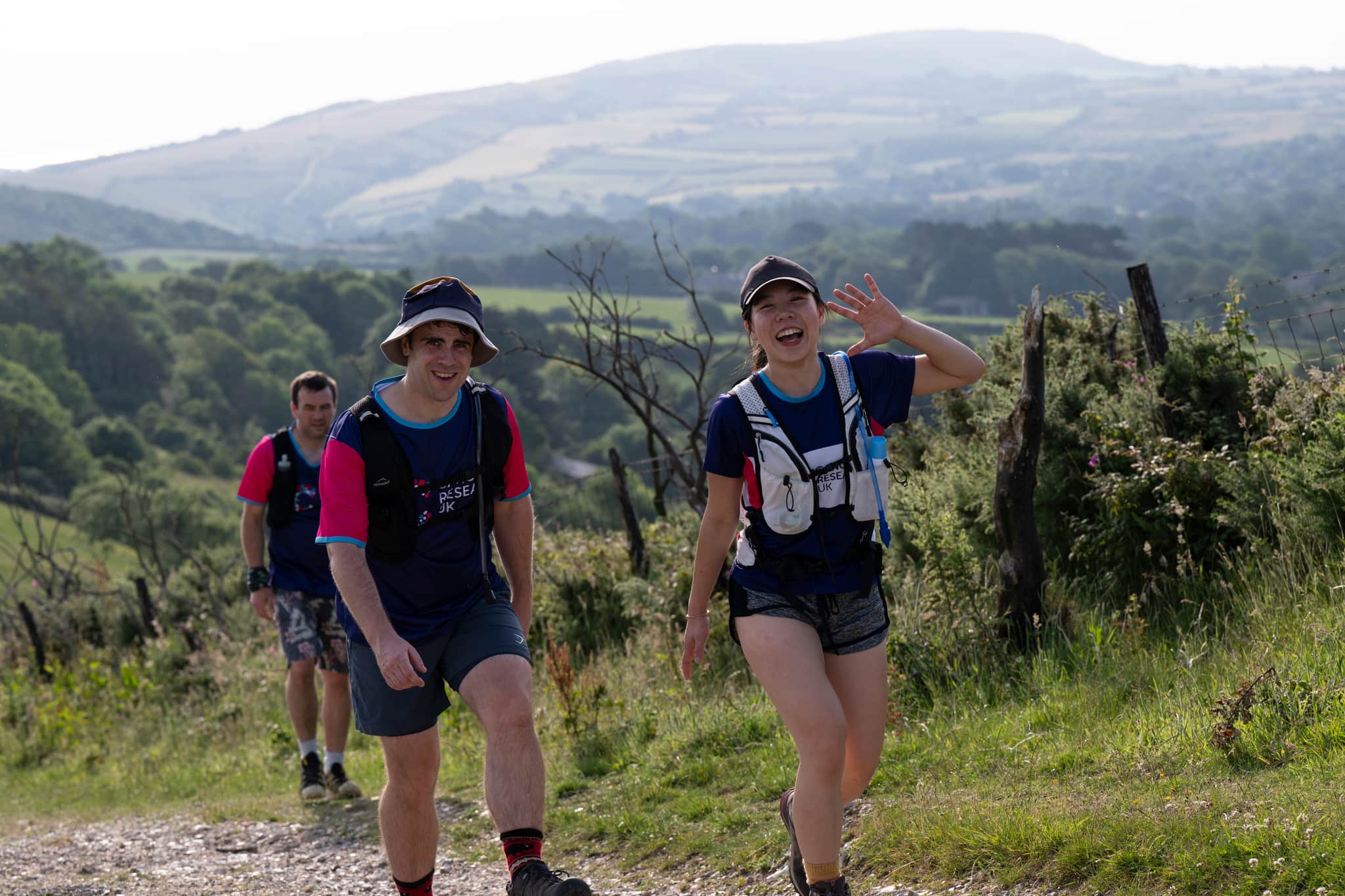 Hikers walking up a hill, smiling and waving at the camera.
