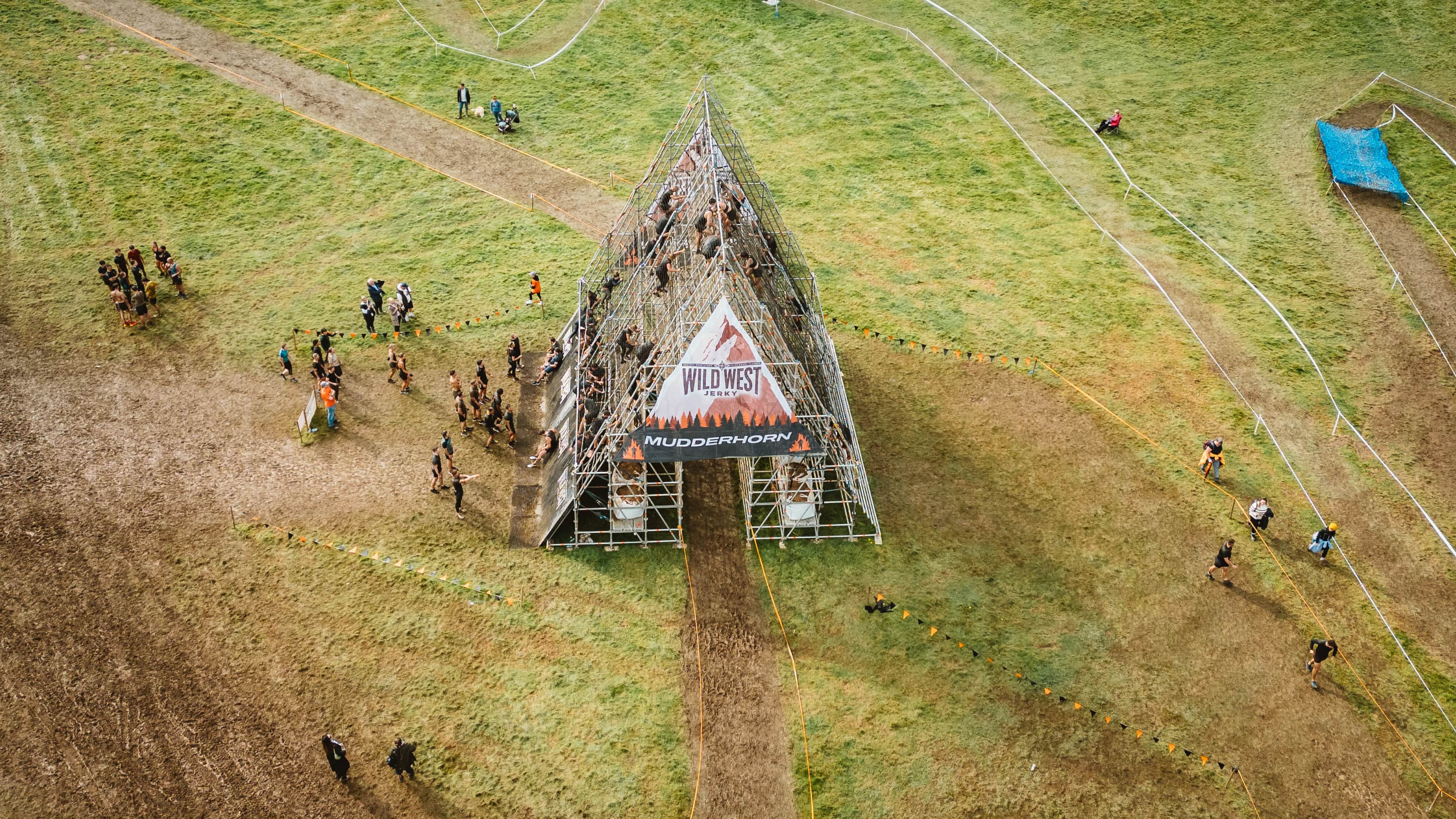 people in the middle of a green field climbing up and going down a metal house shaped structure.