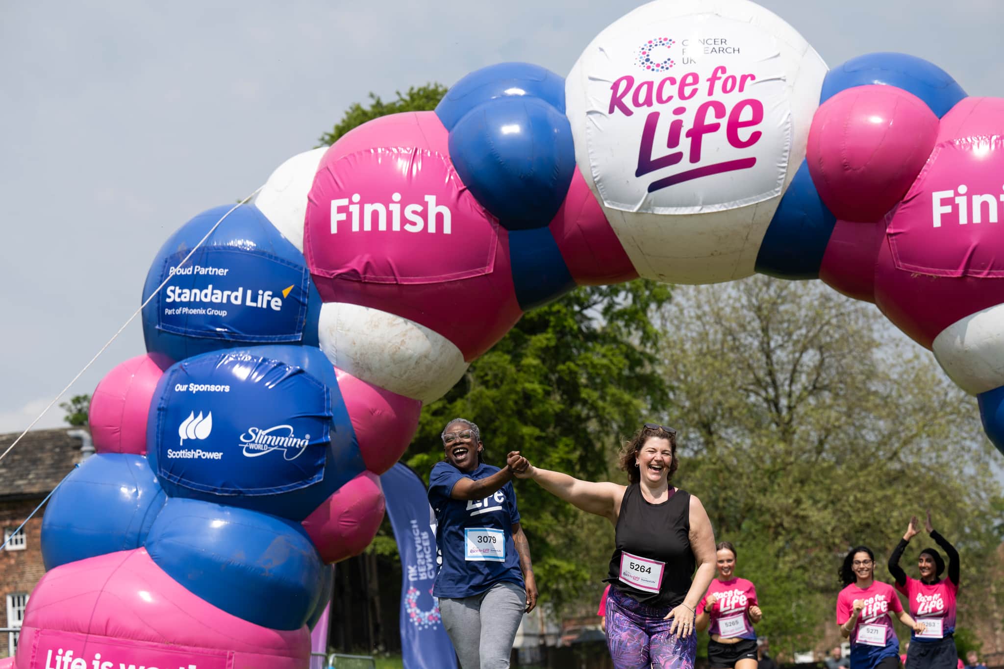 Two people crossing the finishing line at a Race for Life event. They're celebrating.