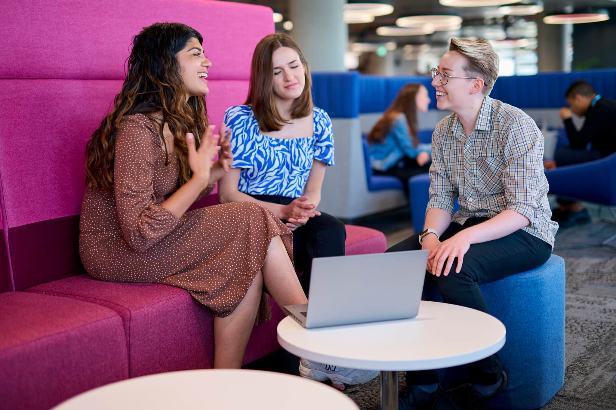 A photo of 5 smiling people chatting in the colourful Cancer Research UK office.