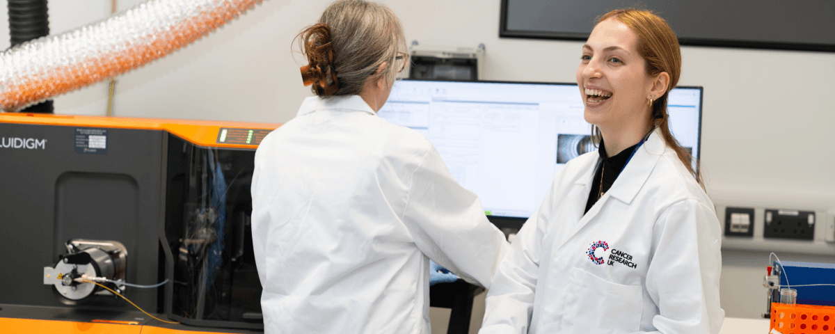 Two researchers in a lab standing at a computer screen working. They look happy.