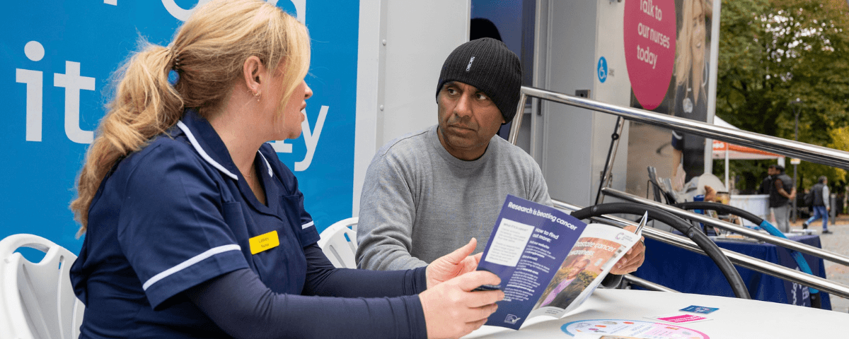 A Cancer Roadshow nurse sits at a table with a man looking at cancer prevention leaflets.