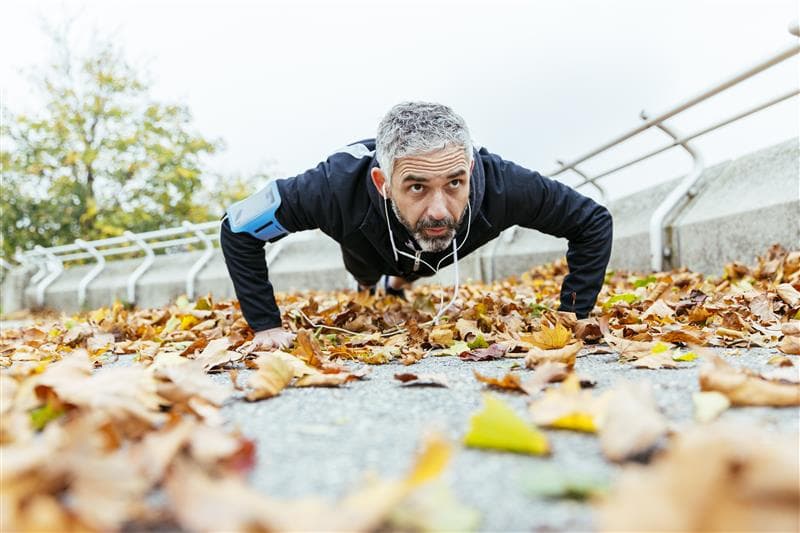 Low-shot of a man doing a push-up on the ground amongst leaves.